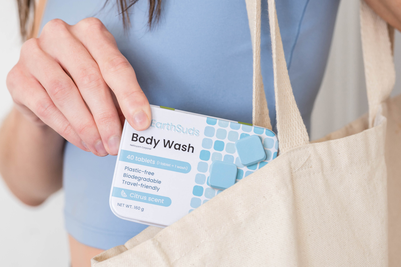 Woman holding EarthSuds plastic-free tin of body wash tablets that are water-free, biodegradable, and eco-friendly in a tote bag.