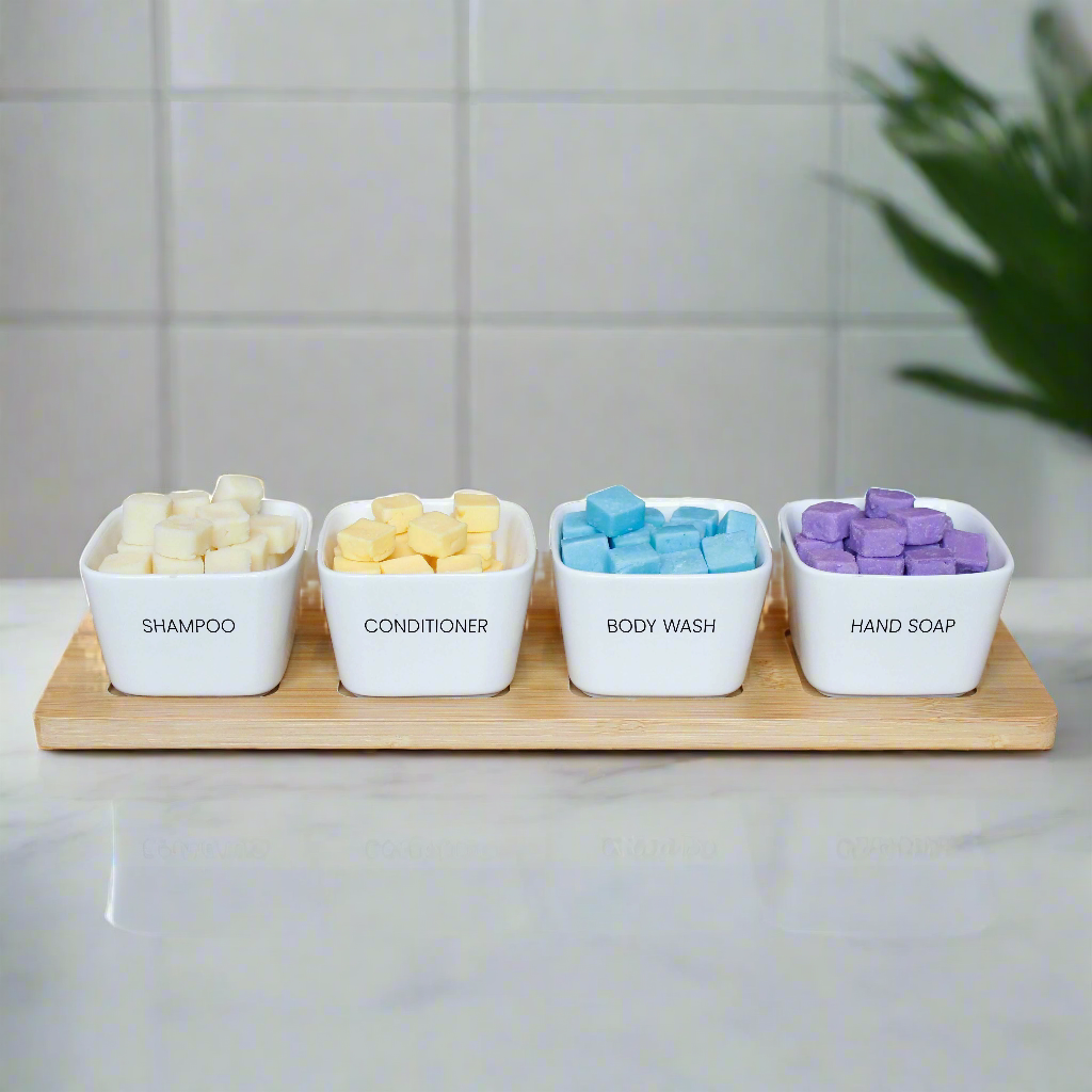 EarthSuds biodegradable shampoo, conditioner, body wash, and hand soap tablets in plastic-free ceramic white bowls on a bamboo tray.