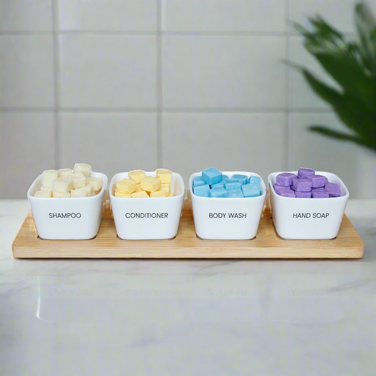 EarthSuds biodegradable shampoo, conditioner, body wash, and hand soap tablets in plastic-free ceramic white bowls on a bamboo tray.