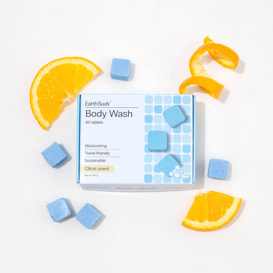 Travel body wash with dissolvable, biodegradable body wash tablets and oranges around it.