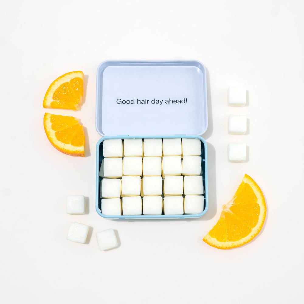 Travel shampoo in case with dissolvable shampoo tablets and oranges around it.