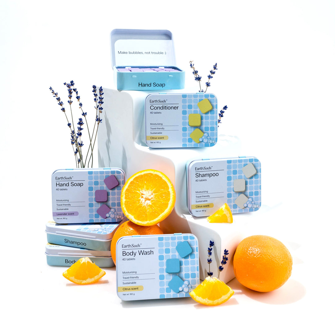 EarthSuds travel shampoo, conditioner, body wash, and hand soap tablets with oranges and lavender on a light background.